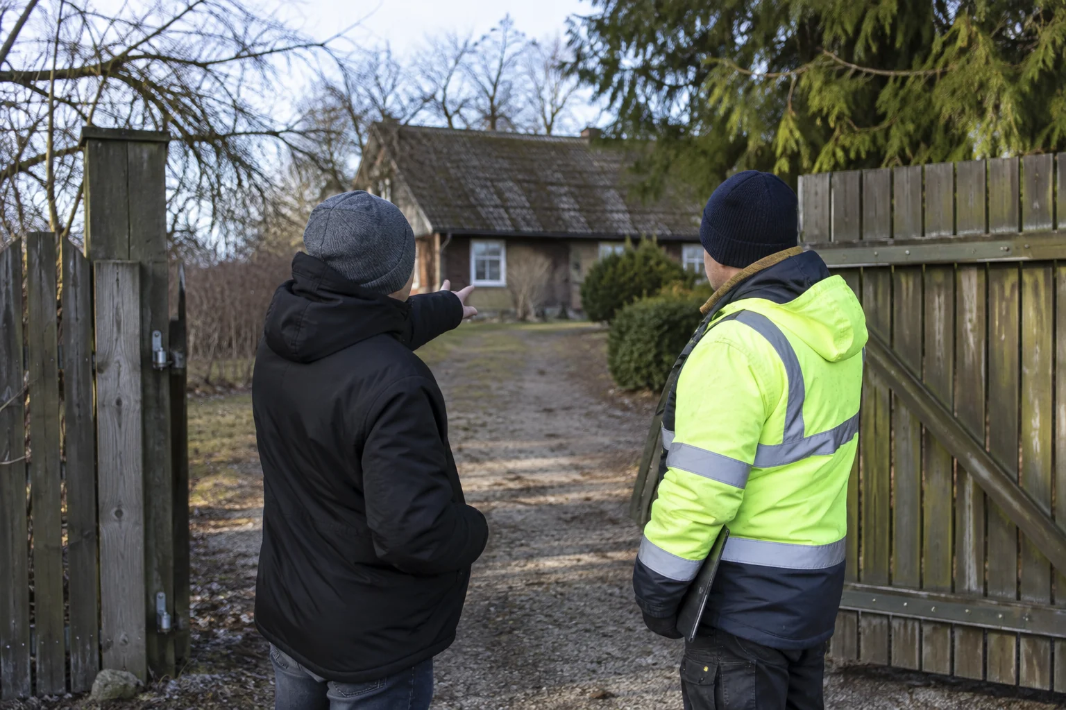 Prie sodybos vartų žmogus su specialistu aptaria privažiavimą prie namo.